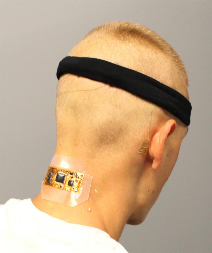 Test subject who has flexible wireless electronics conformed to the back of the neck, with dry hair electrodes under a fabric headband and a membrane electrode on the mastoid, connected with thin-film cables. Source: Woon-Hong Yeo
