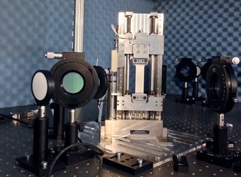 Researchers used a tensile machine to pull a metal specimen with a ceramic thermal barrier coating sprayed on its surface, after which changes in refractive index were measured. Some of the components of the GHz polariscope are seen on either side of the tensile machine. Source: Peter J. Schemmel, Heriot-Watt University