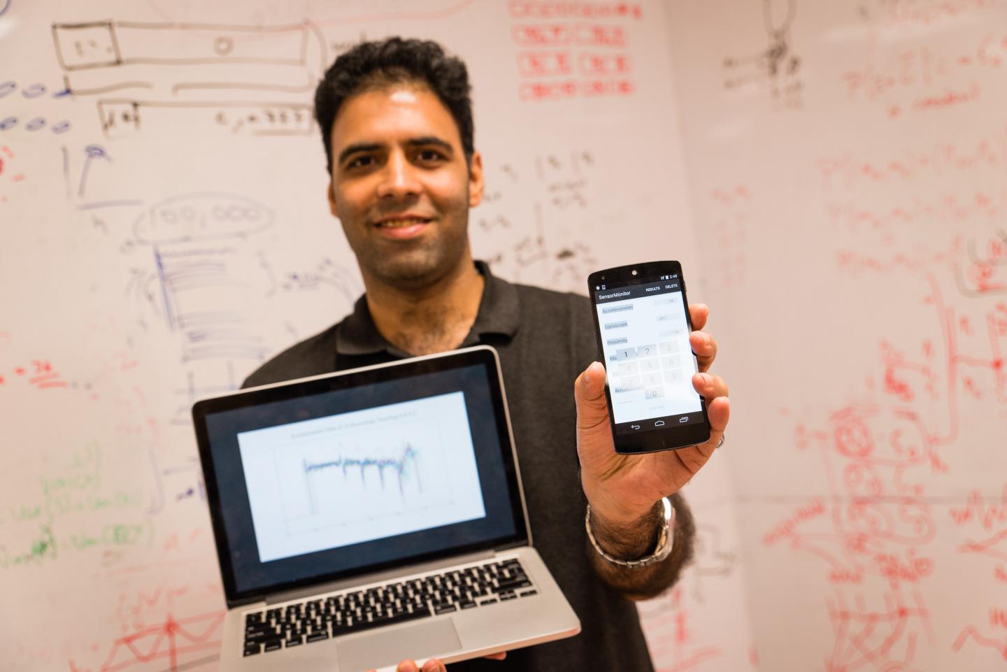 NTU scientist Dr Shivam Bhasin holding a laptop with the deep learning software and a mobile phone with their custom app. Source: NTU Singapore