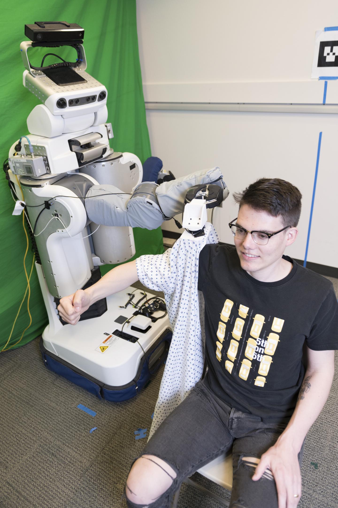 A PR2 robot puts a gown on Henry Clever, a member of the research team. Source: Georgia Tech
