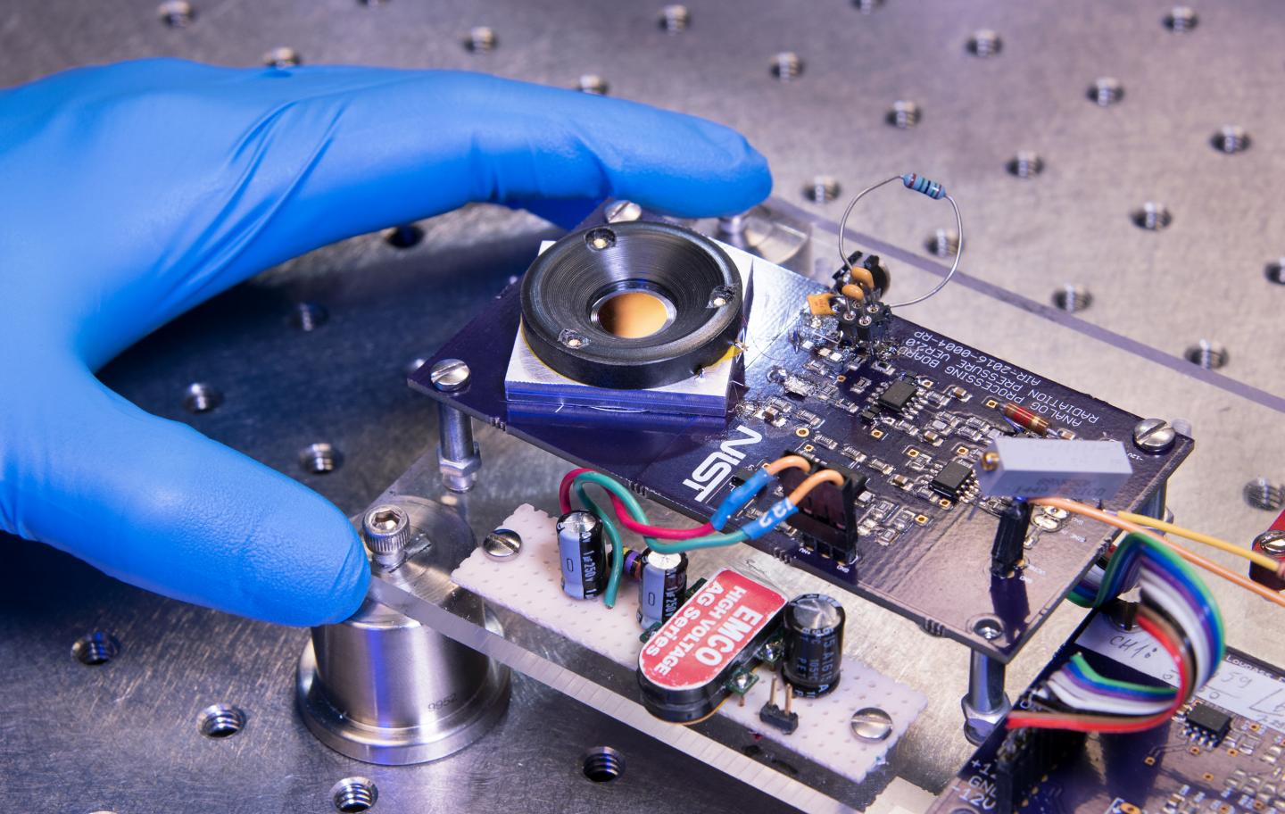A prototype of the smart mirror. Laser light bounces off the highly reflective surface of a silicon plate, visible in the middle of a thick black ring of plastic. Source: Jennifer Lauren Lee/NIST