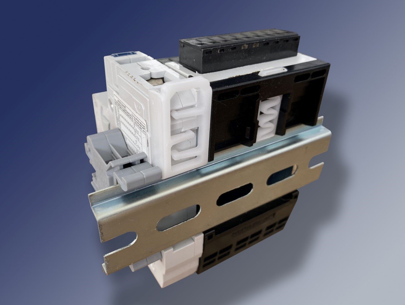 Figure 2. A rear view of a DIN rail with terminal blocks, a circuit breaker and a DIN enclosure mounted on it. They are displayed upside-down for a better view of the latches. Note the release loops at the top of the mounted devices that unclip them. Source: Altech